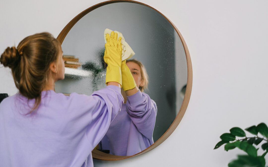 Woman cleaning round mirror with gloves.